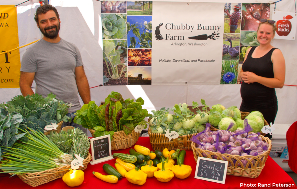 Farmers Michael and Melina of Chubby Bunny Farm with their table of produce at the Phinney Farmers Market.